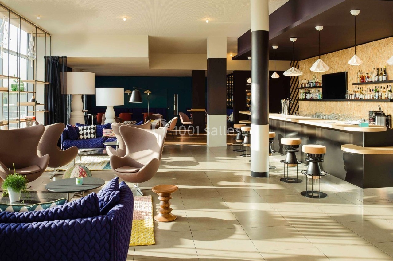 Espace lumineux avec un bar moderne, des fauteuils design et une grande baie vitrée laissant entrer la lumière naturelle.