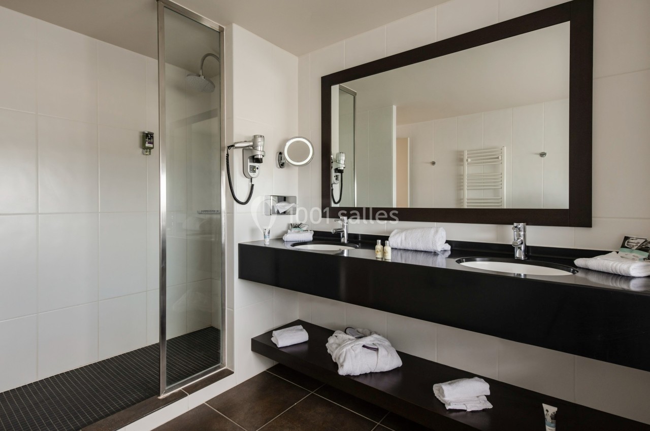 Salle de bain moderne avec douche à l'italienne, double vasque, miroir encadré et serviettes disposées sur les étagères.
