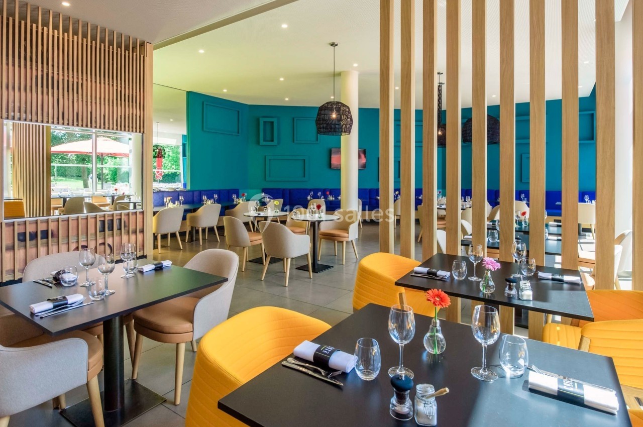 Salle de restaurant moderne avec tables dressées, chaises colorées et décoration murale bleu vif.