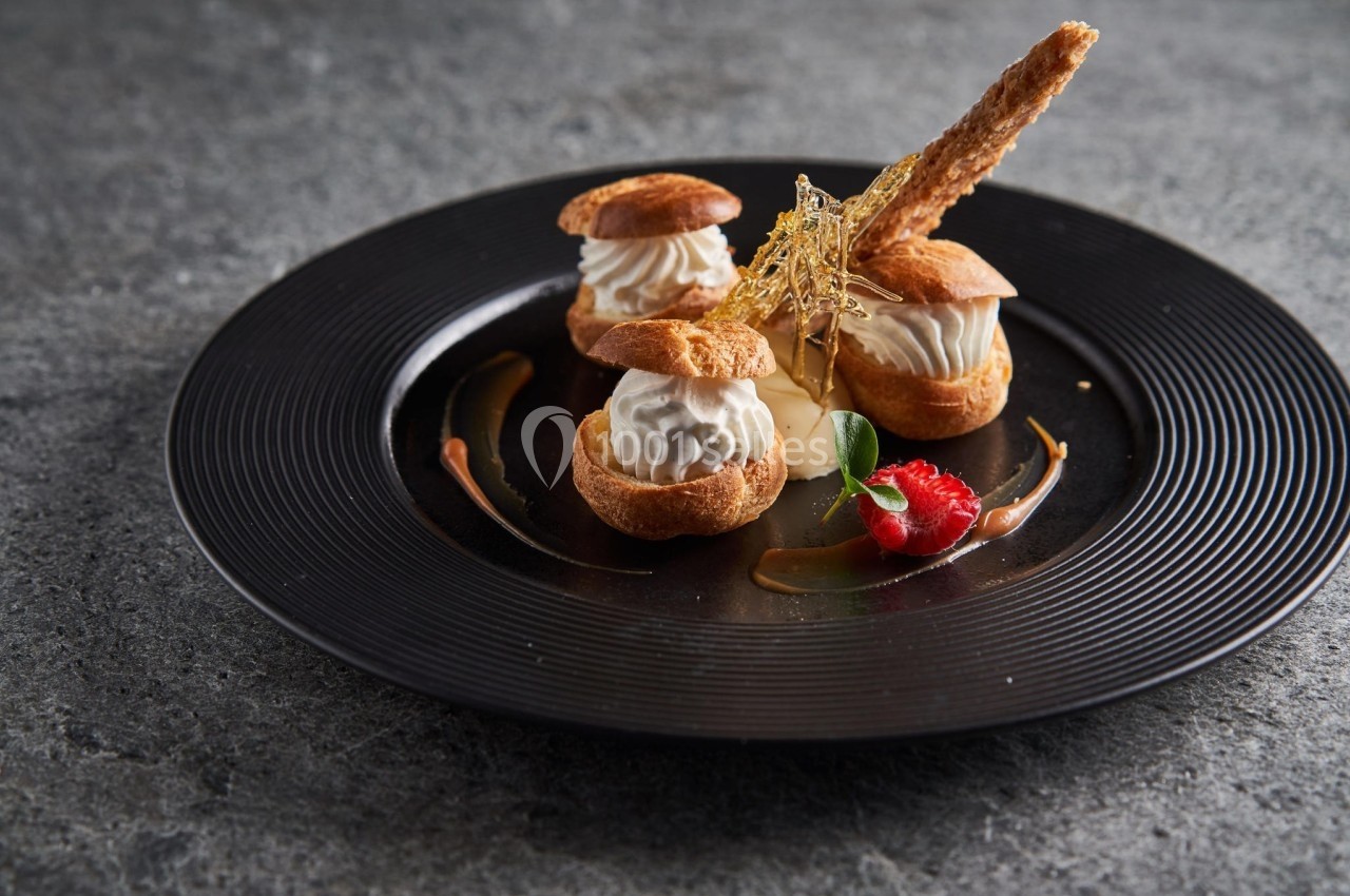 Assiette de profiteroles garnies de crème, décorées de caramel filé, d'une framboise et d'une feuille verte.