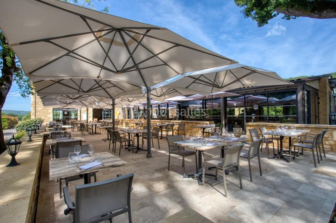 Terrasse d'un restaurant avec tables dressées sous de grands parasols, entourée de verdure et baignée de lumière naturelle.