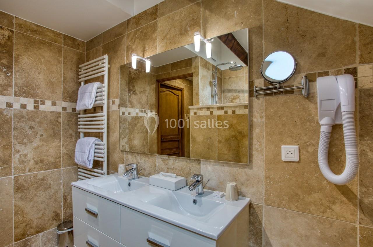 Salle de bain avec double vasque, miroir éclairé, sèche-serviettes, sèche-cheveux et carrelage beige.