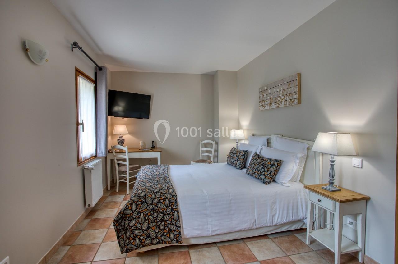 Chambre lumineuse avec lit double, décor sobre, bureau, télévision murale et deux lampes de chevet allumées.