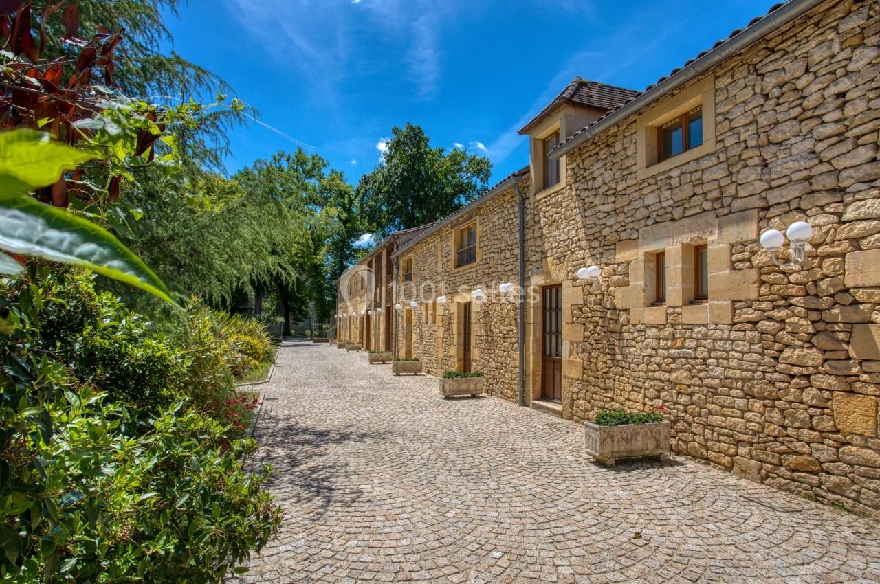 Façade en pierre d'un bâtiment avec allée pavée bordée de végétation sous un ciel bleu.