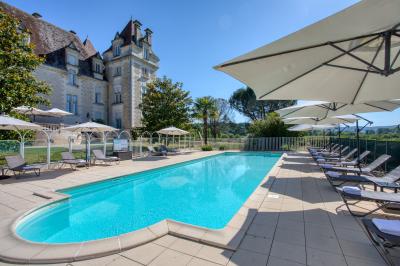Façade d'un château en pierre entouré de végétation, avec un ciel bleu partiellement nuageux en arrière-plan.