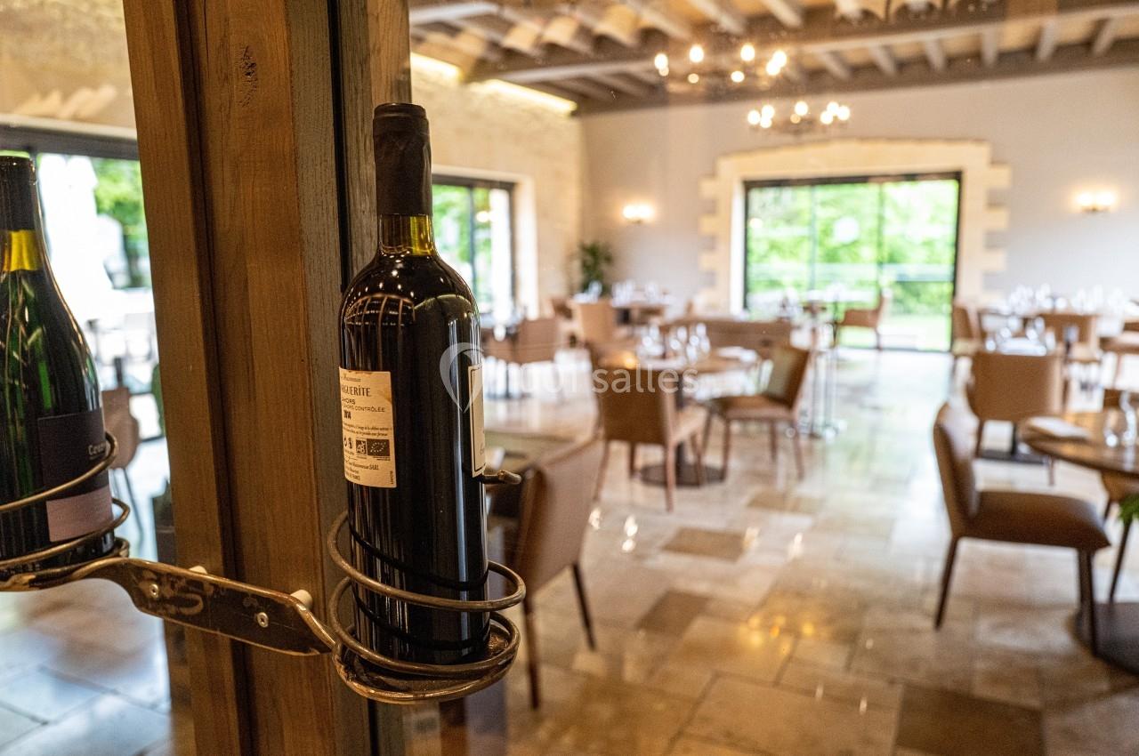 Bouteille de vin rouge accrochée à une structure en métal dans un restaurant lumineux avec des tables dressées.
