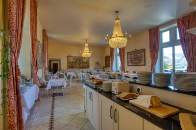 Façade d'un château en pierre entouré de végétation, avec un ciel bleu partiellement nuageux en arrière-plan.