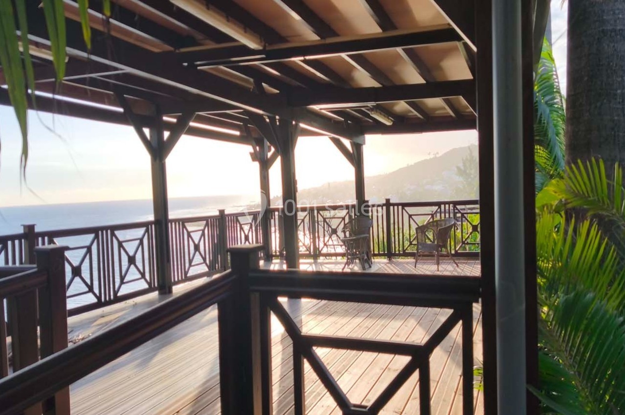 Terrasse en bois avec vue sur la mer au coucher du soleil, entourée de végétation tropicale.