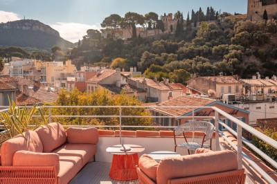 Miniature Location salle Cassis (Bouches-du-Rhône) - Hôtel Liautaud Cassis #5 Salon lumineux avec canapé beige incurvé, chaises en bois, tables basses rondes et plantes en pot près de grandes fenêtres.
