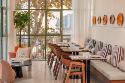 Miniature Location salle Cassis (Bouches-du-Rhône) - Hôtel Liautaud Cassis #2 Salon lumineux avec canapé beige incurvé, chaises en bois, tables basses rondes et plantes en pot près de grandes fenêtres.