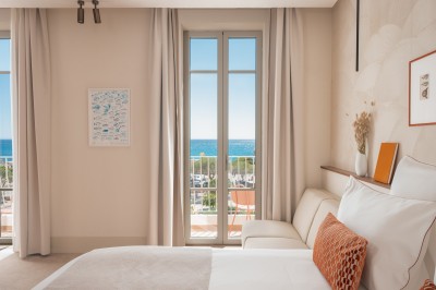 Miniature Location salle Cassis (Bouches-du-Rhône) - Hôtel Liautaud Cassis #8 Salon lumineux avec canapé beige incurvé, chaises en bois, tables basses rondes et plantes en pot près de grandes fenêtres.