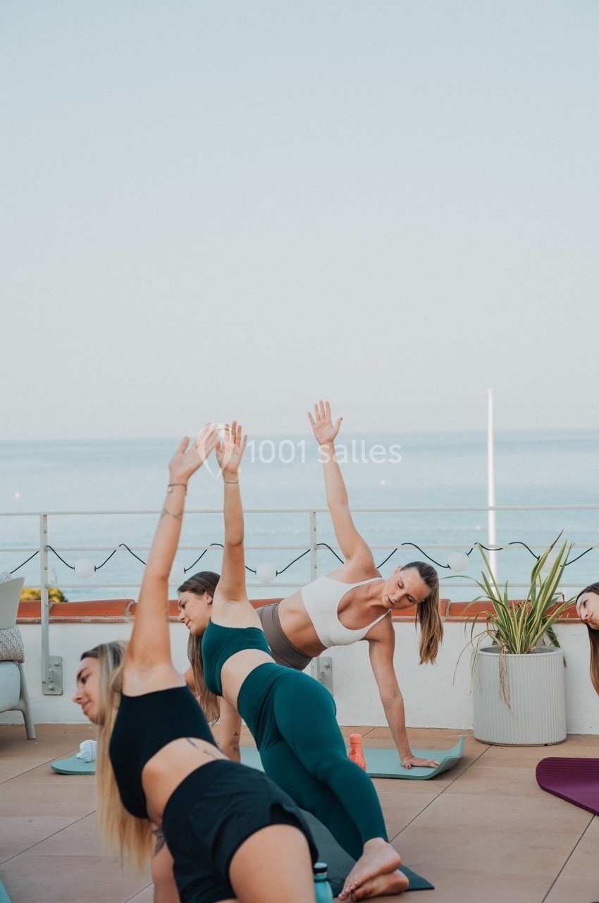 Des personnes pratiquent le yoga en plein air sur une terrasse avec vue sur la mer, par temps clair.