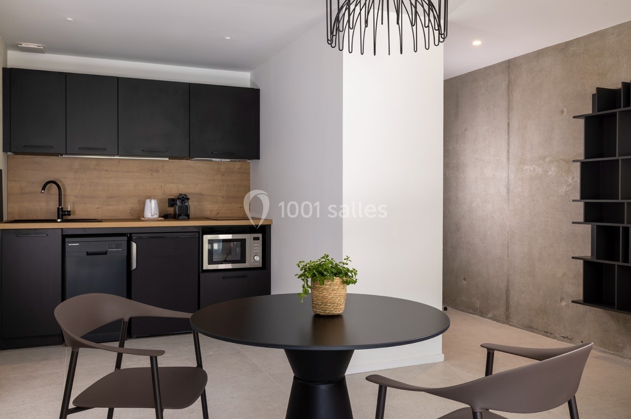 Cuisine moderne avec meubles noirs, table ronde noire, chaises assorties et mur en béton brut en arrière-plan.