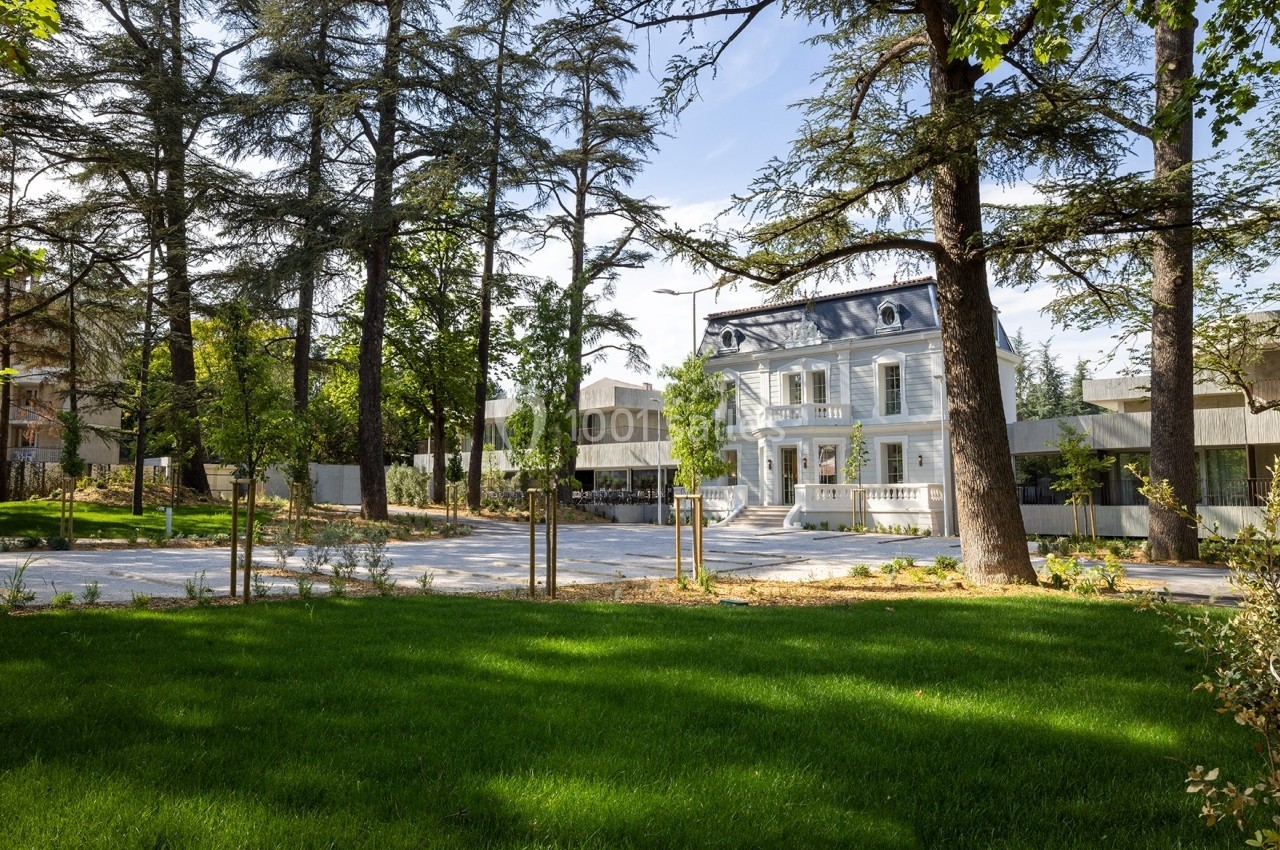 Façade d'une maison blanche entourée d'arbres et d'un jardin verdoyant sous un ciel dégagé.