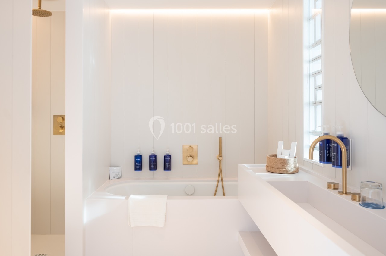 Salle de bain lumineuse avec baignoire, robinetterie dorée, douche à l'italienne et étagères blanches.