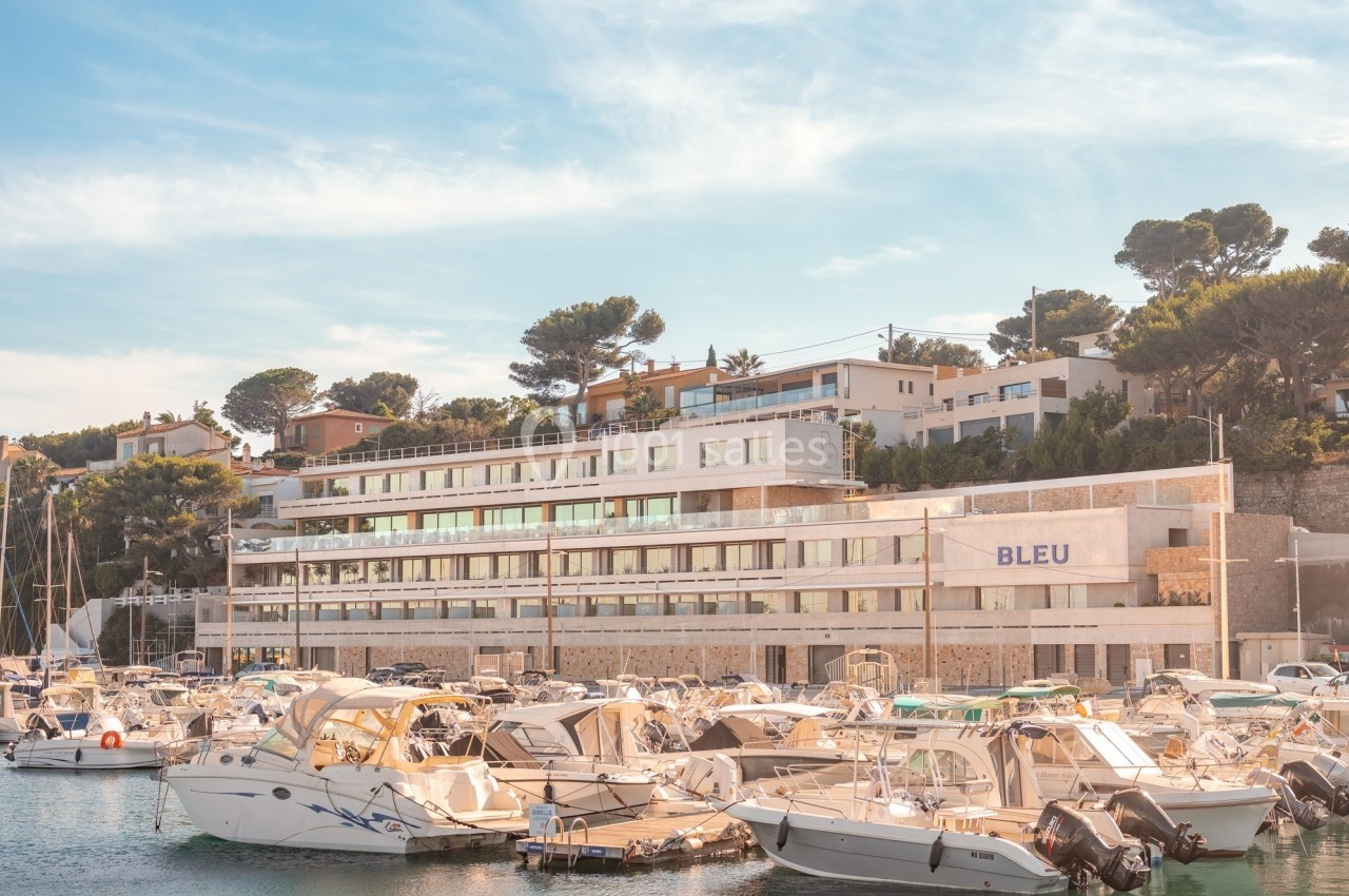 Vue d'un port de plaisance avec des bateaux amarrés devant un bâtiment moderne entouré de végétation.