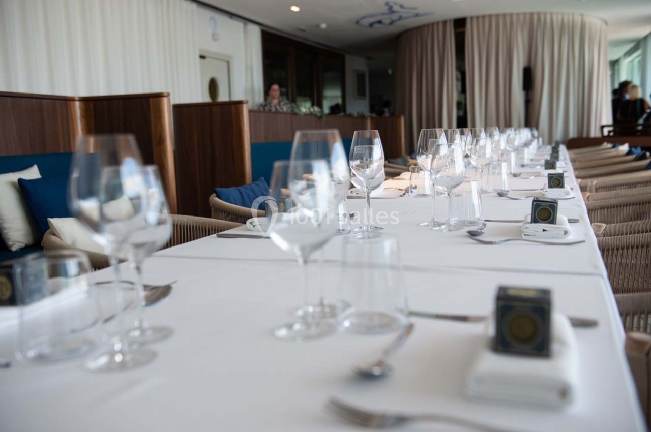 Table dressée avec nappes blanches, verres à pied, couverts et serviettes dans une salle lumineuse et élégante.