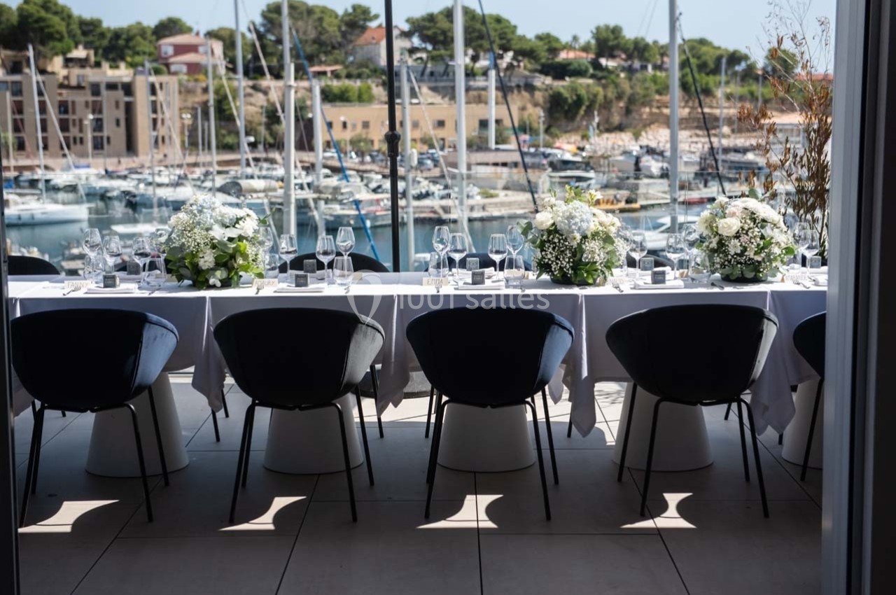 Table élégamment dressée avec des fleurs blanches, vue sur un port de plaisance en arrière-plan.