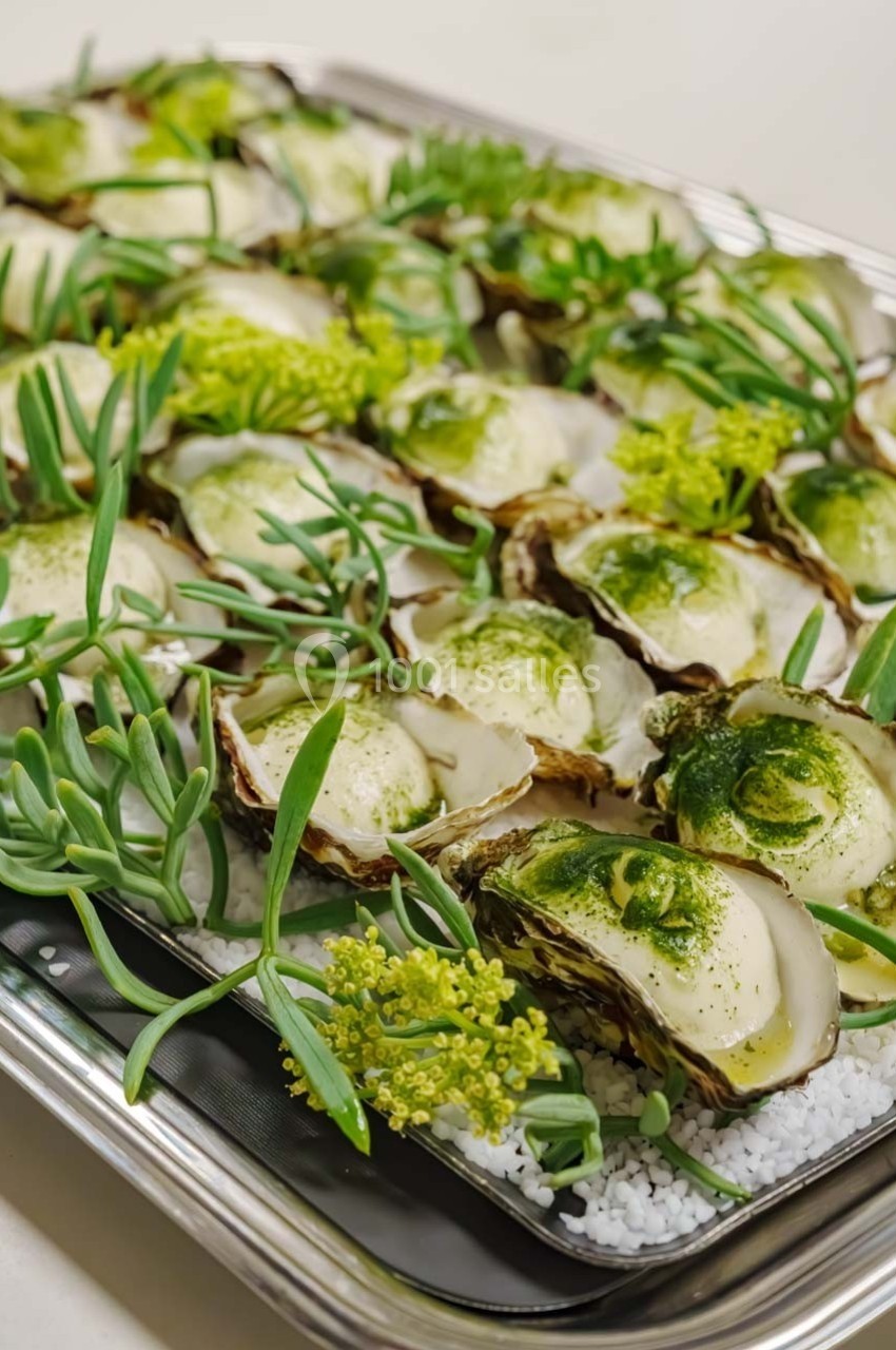 Plateau d'huîtres garnies de crème et d'herbes, décoré de plantes vertes et présenté sur un lit de sel.