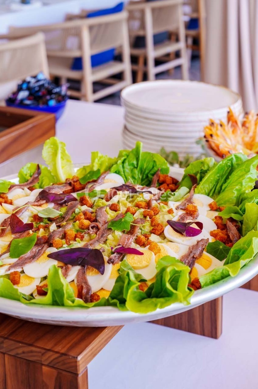 Salade composée avec laitue, œufs durs, anchois, croûtons et garnitures colorées, présentée sur une table dressée.