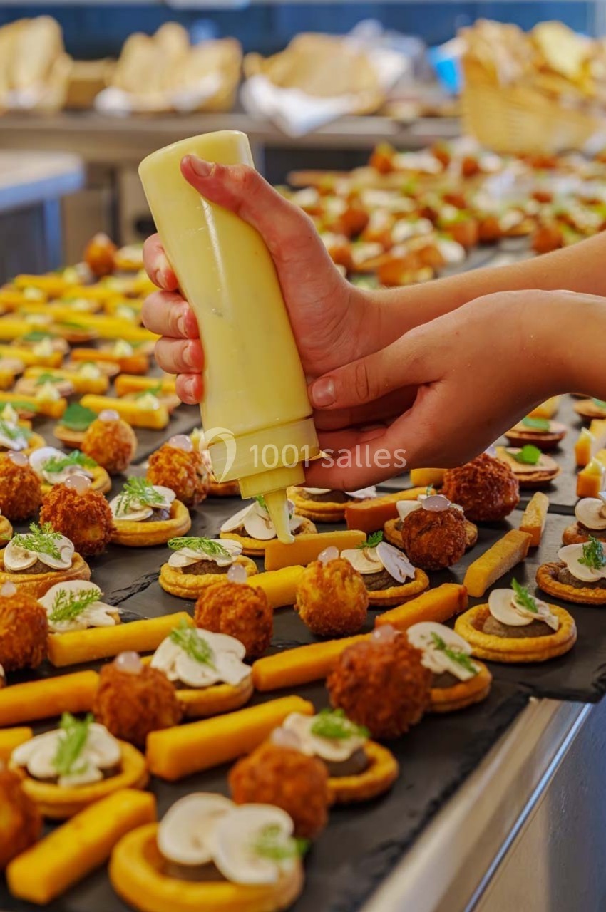 Des mains dressent des amuse-bouches sur des ardoises, ajoutant une sauce avec une bouteille en cuisine.