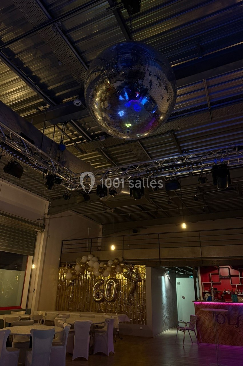 Salle décorée pour un 60e anniversaire avec une grande boule disco suspendue et des ballons dorés en arrière-plan.