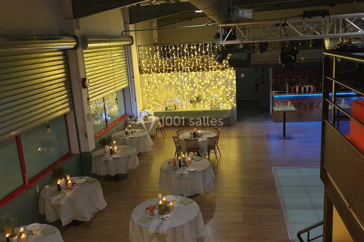 Salle de réception avec tables rondes dressées, éclairage tamisé et guirlandes lumineuses en arrière-plan.