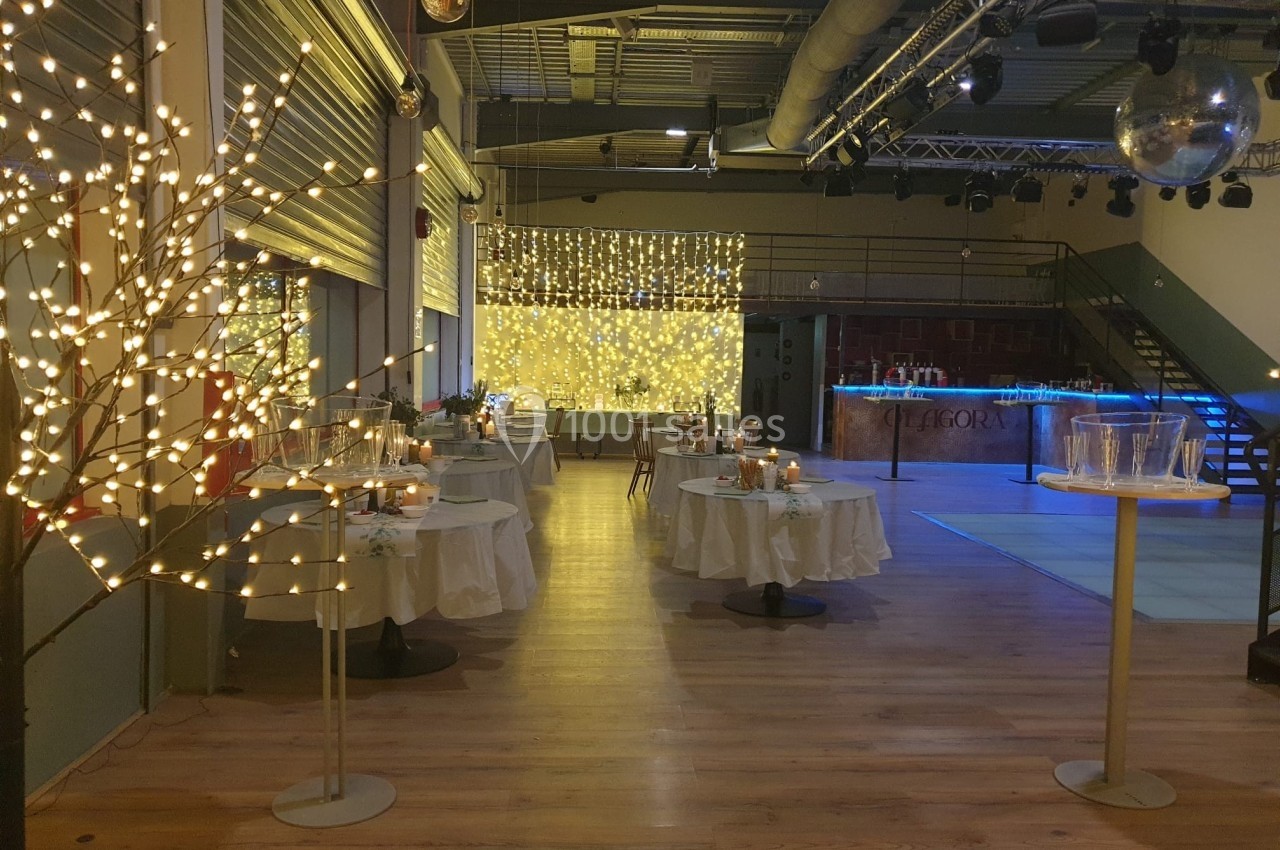 Salle de réception décorée avec des guirlandes lumineuses, tables dressées et piste de danse éclairée.