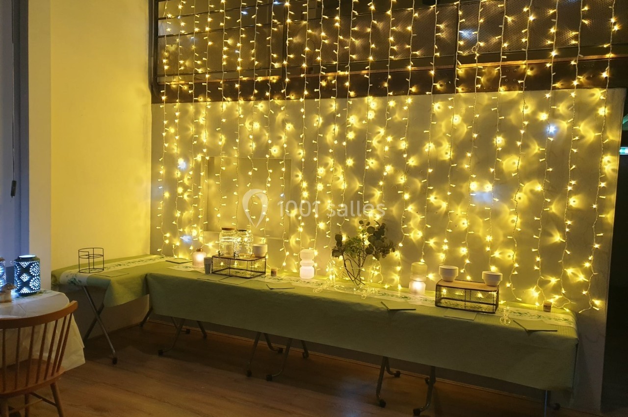Guirlandes lumineuses dorées illuminant une table décorée avec des bougies et des fleurs dans une pièce chaleureuse.