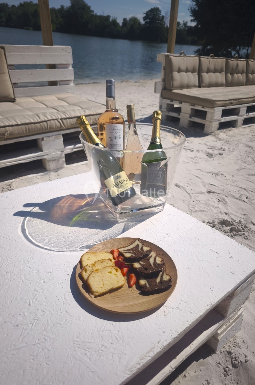 Plateau avec pain, charcuterie et fraises sur une table blanche, accompagné de bouteilles dans un seau à glace, en bord de…