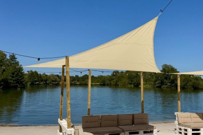 Deux personnes debout dans l'eau peu profonde d'un lac, tenant des verres, avec des arbres et un ciel bleu en arrière-plan.