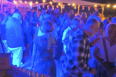 Deux personnes debout dans l'eau peu profonde d'un lac, tenant des verres, avec des arbres et un ciel bleu en arrière-plan.
