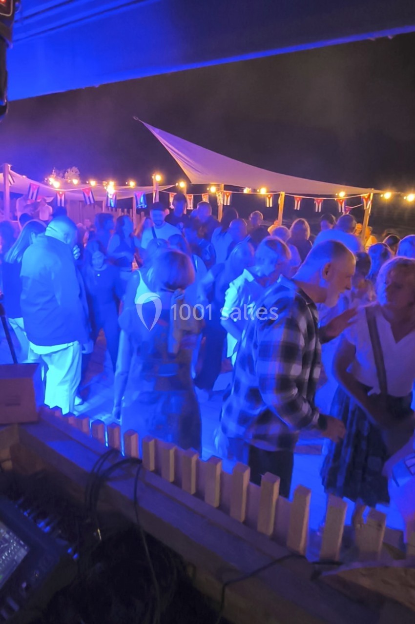 Groupe de personnes dansant et discutant sous un éclairage bleu lors d'un événement en plein air en soirée.