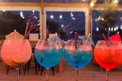 Terrasse d'un restaurant avec voiles d'ombrage, mobilier en bois, vue sur un étang et ambiance estivale.