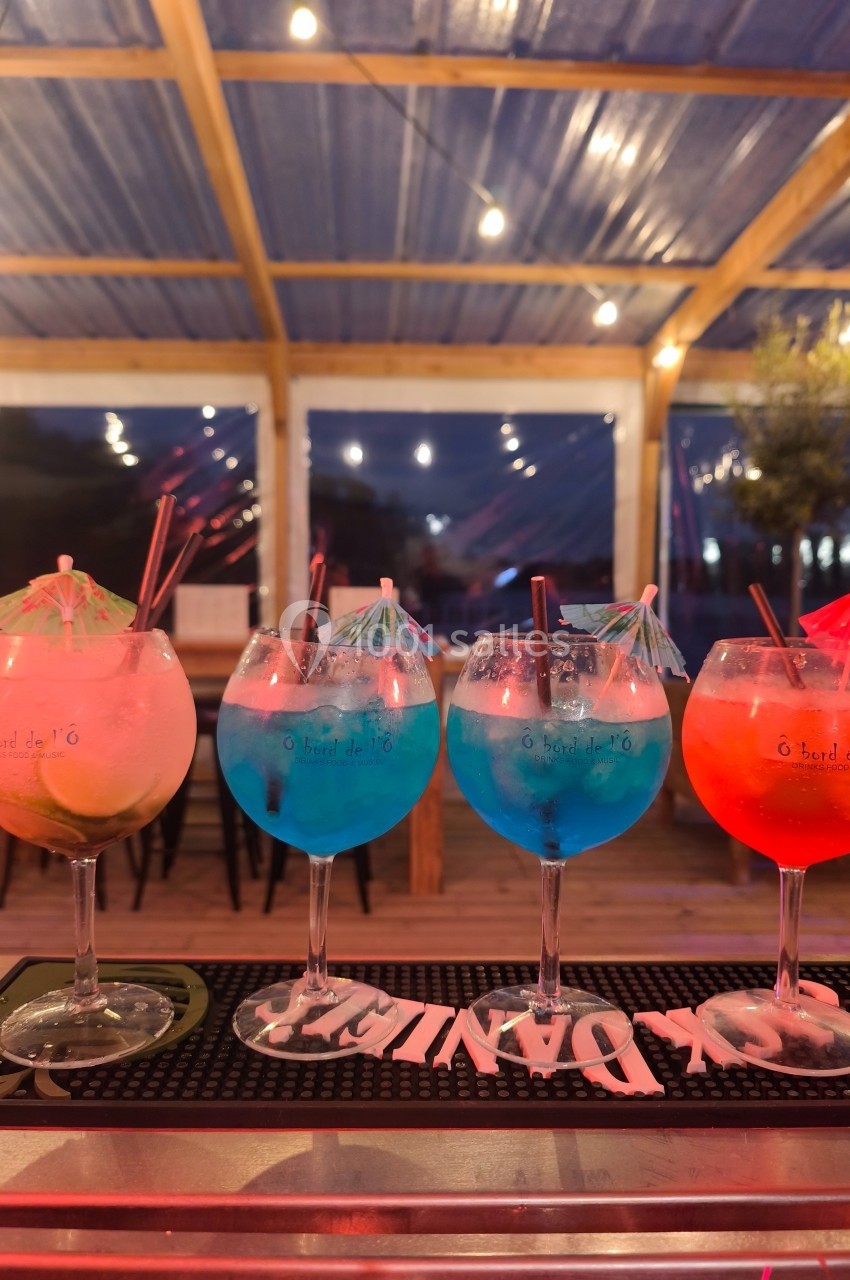 Quatre cocktails colorés avec glaçons et décorations en parasol sur un comptoir, en terrasse éclairée le soir.