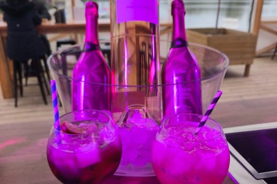 Terrasse d'un restaurant avec voiles d'ombrage, mobilier en bois, vue sur un étang et ambiance estivale.