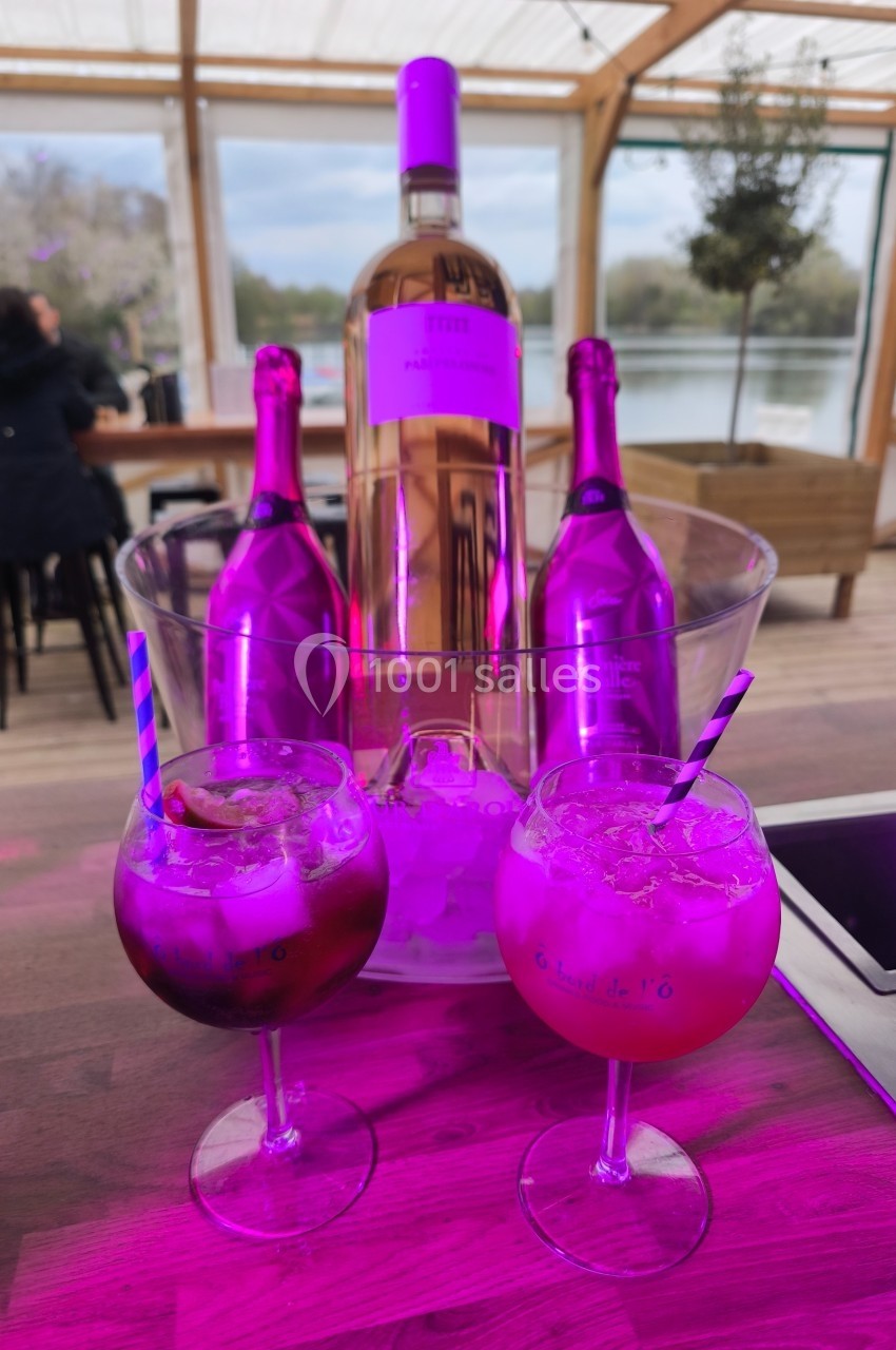 Deux verres de cocktails colorés posés sur une table en bois, avec des bouteilles de vin rosé dans un seau à glace en…