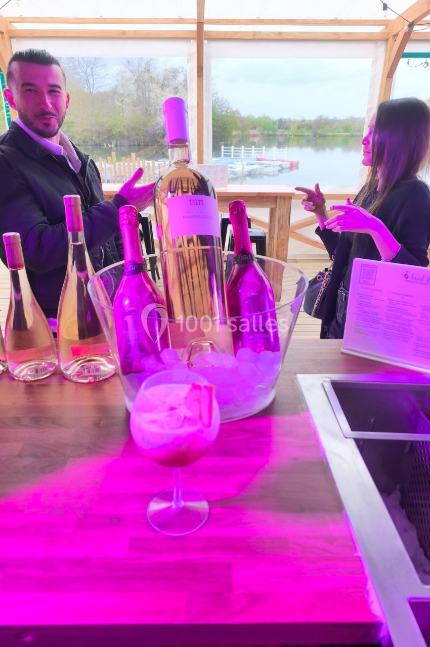 Deux personnes discutent près d'une table avec des bouteilles de vin rosé et un seau à glace, en extérieur.