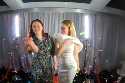 Miniature 58 Vidéo Photographie #3 Deux femmes souriantes dansent sous des confettis colorés, devant un rideau gris et des cordons de sécurité rouges.