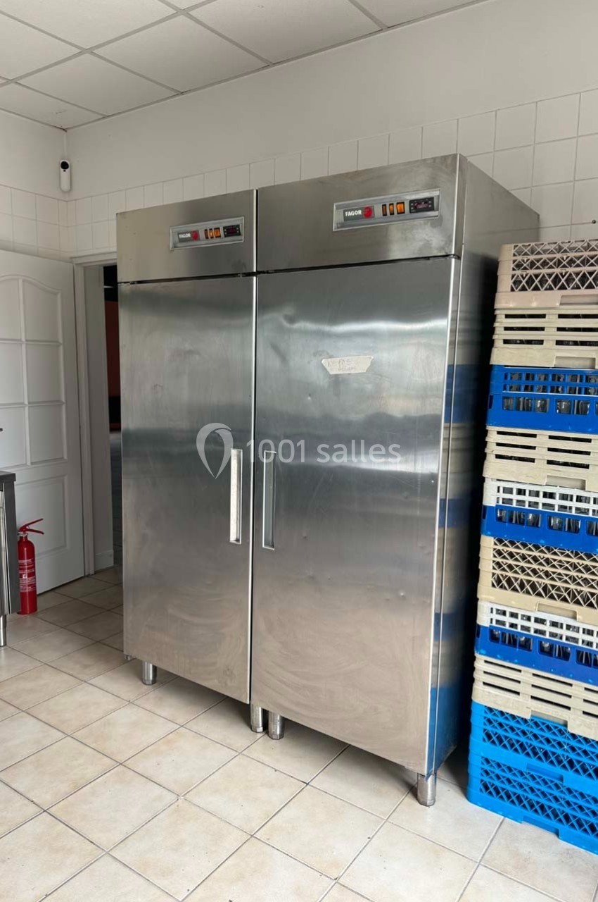 Deux grandes armoires réfrigérées en acier inoxydable dans une pièce carrelée avec des caisses empilées à droite.