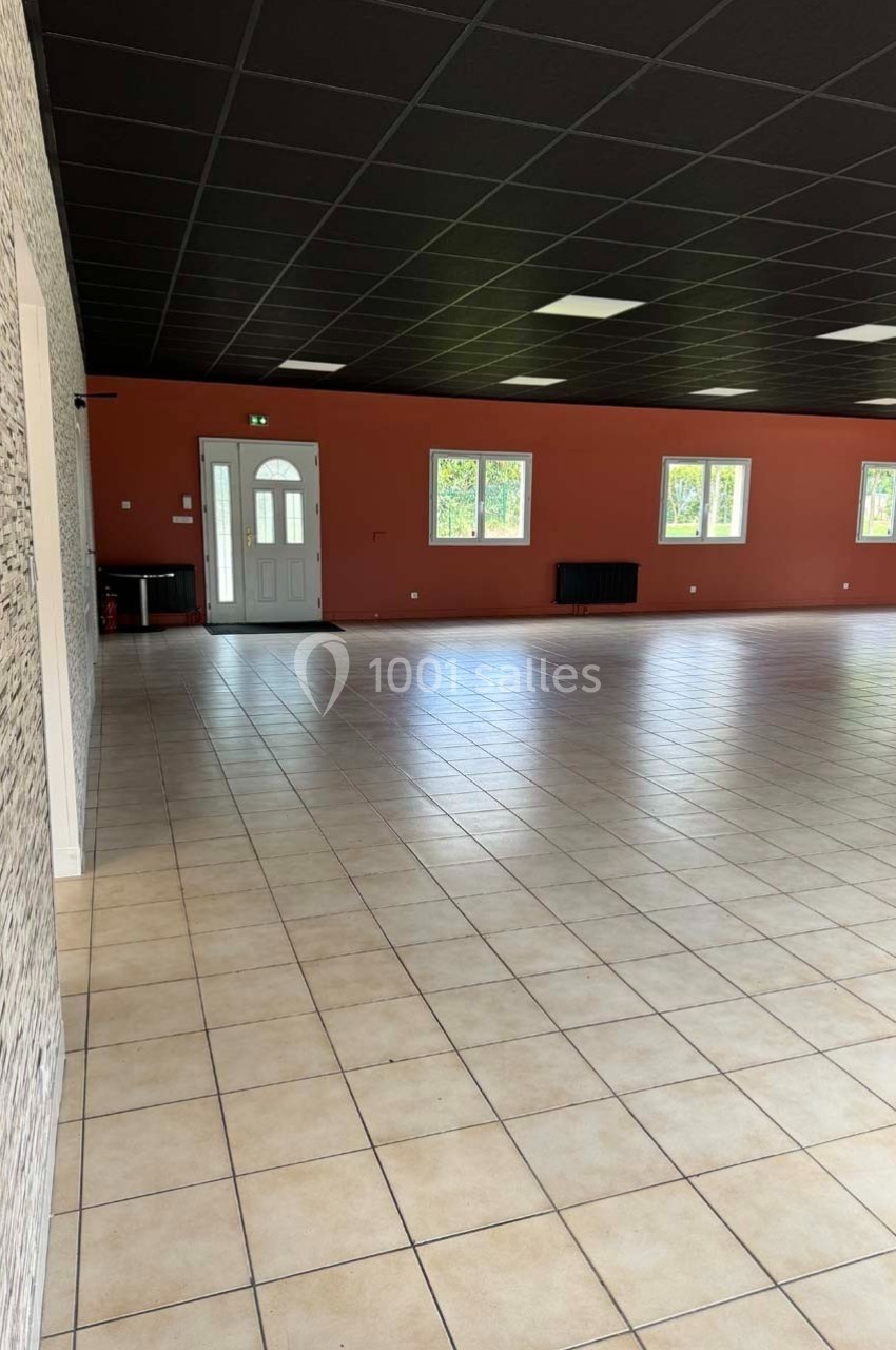 Salle vide avec carrelage beige, murs rouges et blancs, plafond noir, fenêtres alignées et porte d'entrée vitrée.