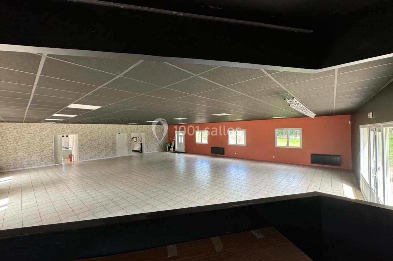 Salle spacieuse avec carrelage clair, murs rouges et en pierre, grandes fenêtres laissant entrer la lumière naturelle.