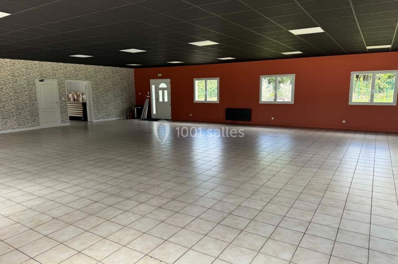 Salle spacieuse avec carrelage clair, murs rouges et blancs, plafond noir et plusieurs fenêtres laissant entrer la lumière.