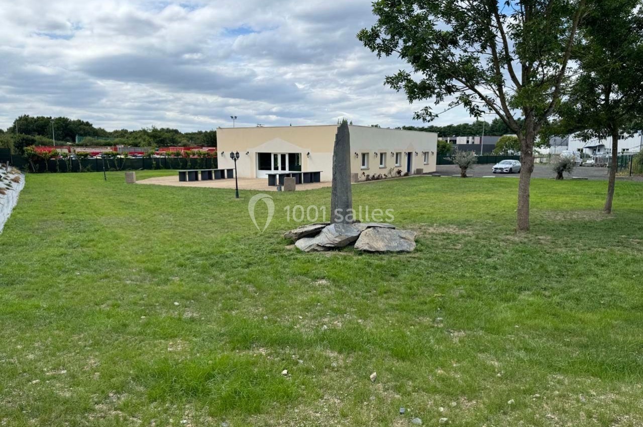 Bâtiment moderne de plain-pied entouré d'une pelouse, avec un arbre et des pierres au premier plan.