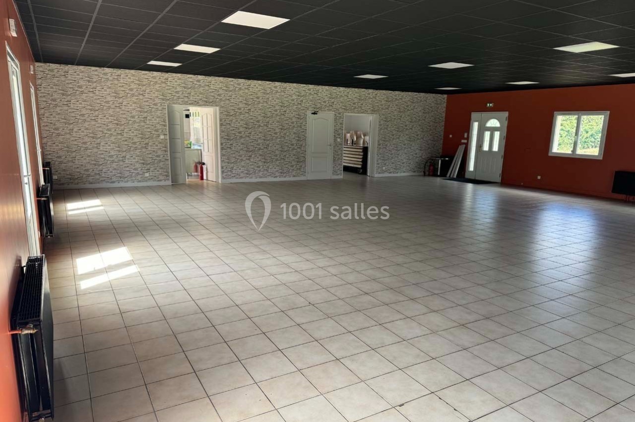 Salle spacieuse avec carrelage clair, murs orange et gris, plafond noir, éclairée par des fenêtres et des luminaires.