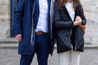 Un couple s'embrasse dans une rue pavée devant un bâtiment rose couvert de végétation.