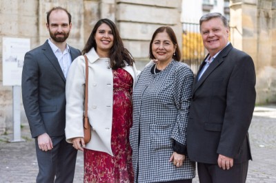 Un couple s'embrasse dans une rue pavée devant un bâtiment rose couvert de végétation.