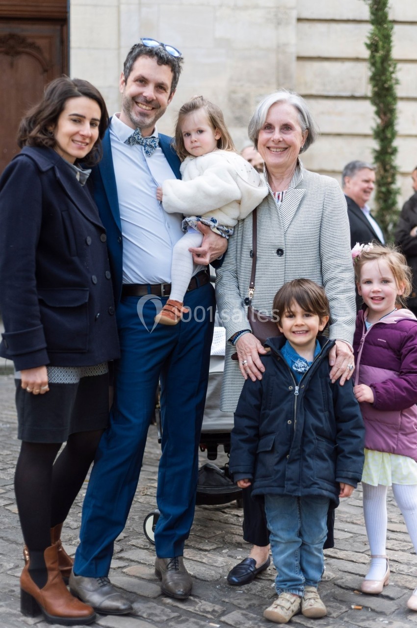 Un groupe de personnes, composé d'adultes et d'enfants, pose souriants devant un bâtiment en pierre.