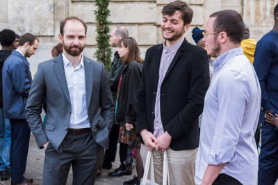 Un couple s'embrasse dans une rue pavée devant un bâtiment rose couvert de végétation.