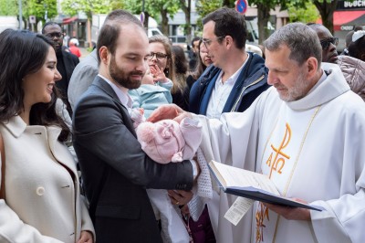 Un couple s'embrasse dans une rue pavée devant un bâtiment rose couvert de végétation.